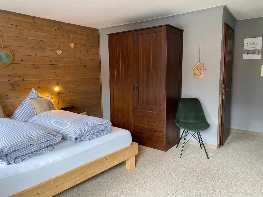 A bedroom with a wooden bed, a wardrobe, a green chair, and a wall with heart decorations.