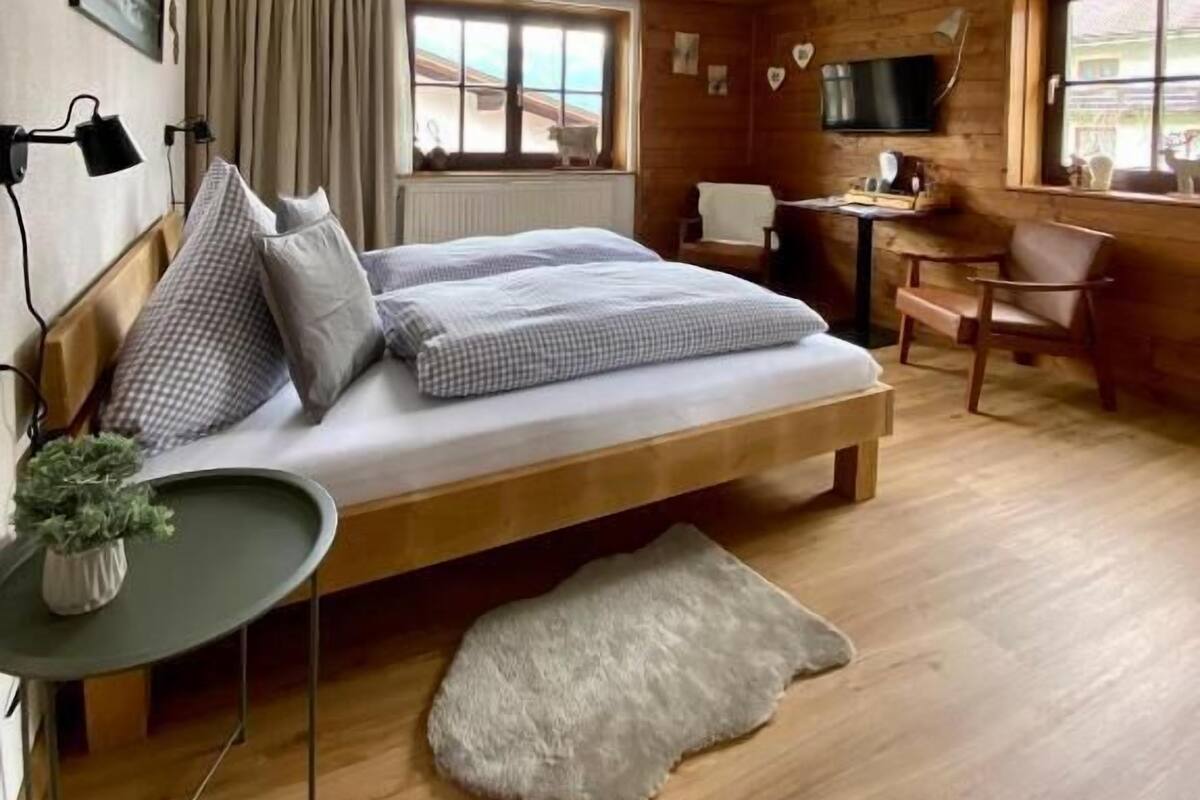 A cozy bedroom with a wooden bed, a small table, a chair, and a television.