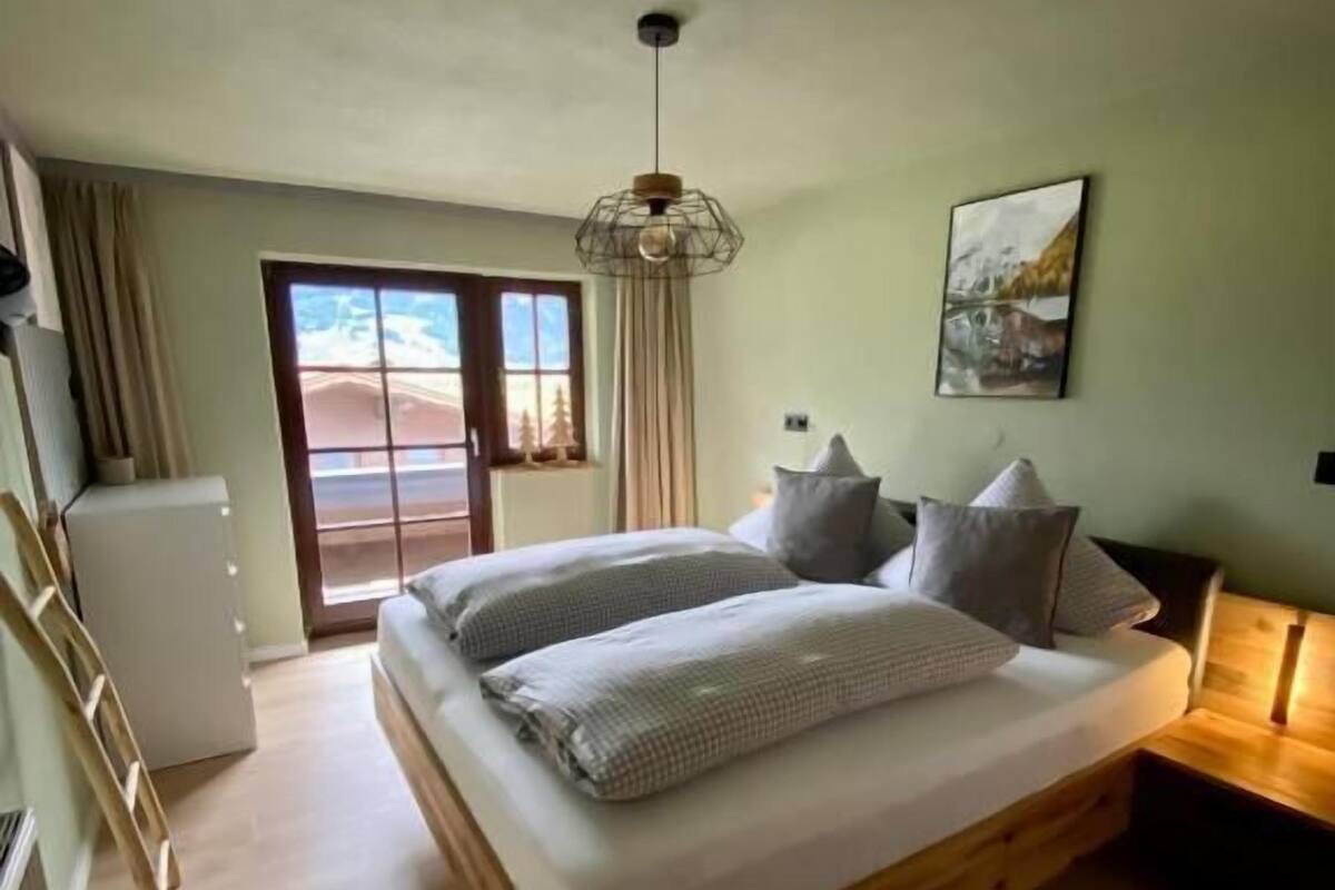 A bedroom with a wooden bed, a desk, a chair, a wardrobe, and a view of the outdoors.