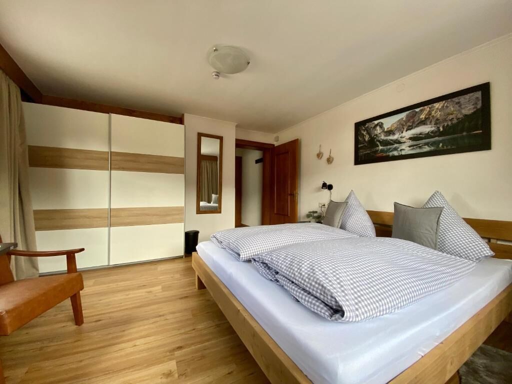 A bedroom with a bed, a chair, a wardrobe, and a painting on the wall.