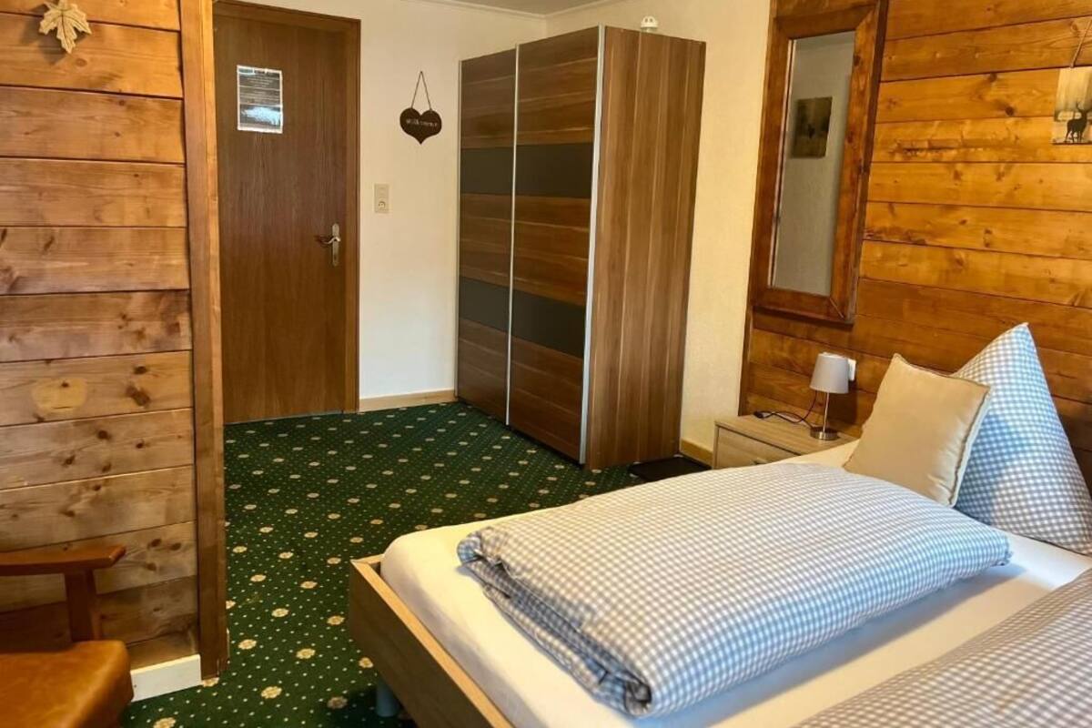 A room with a bed, wooden wardrobe, and a mirror.
