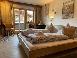 A hotel room with a large bed, a desk, a chair, and a window with curtains. - Haus Tirol Ehrwald (Ehrwald)