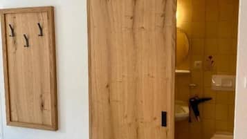 Ein Zimmer mit Holztür zum Badezimmer, einem Holzkabinet mit Haken und einem Bett mit Kissen.
