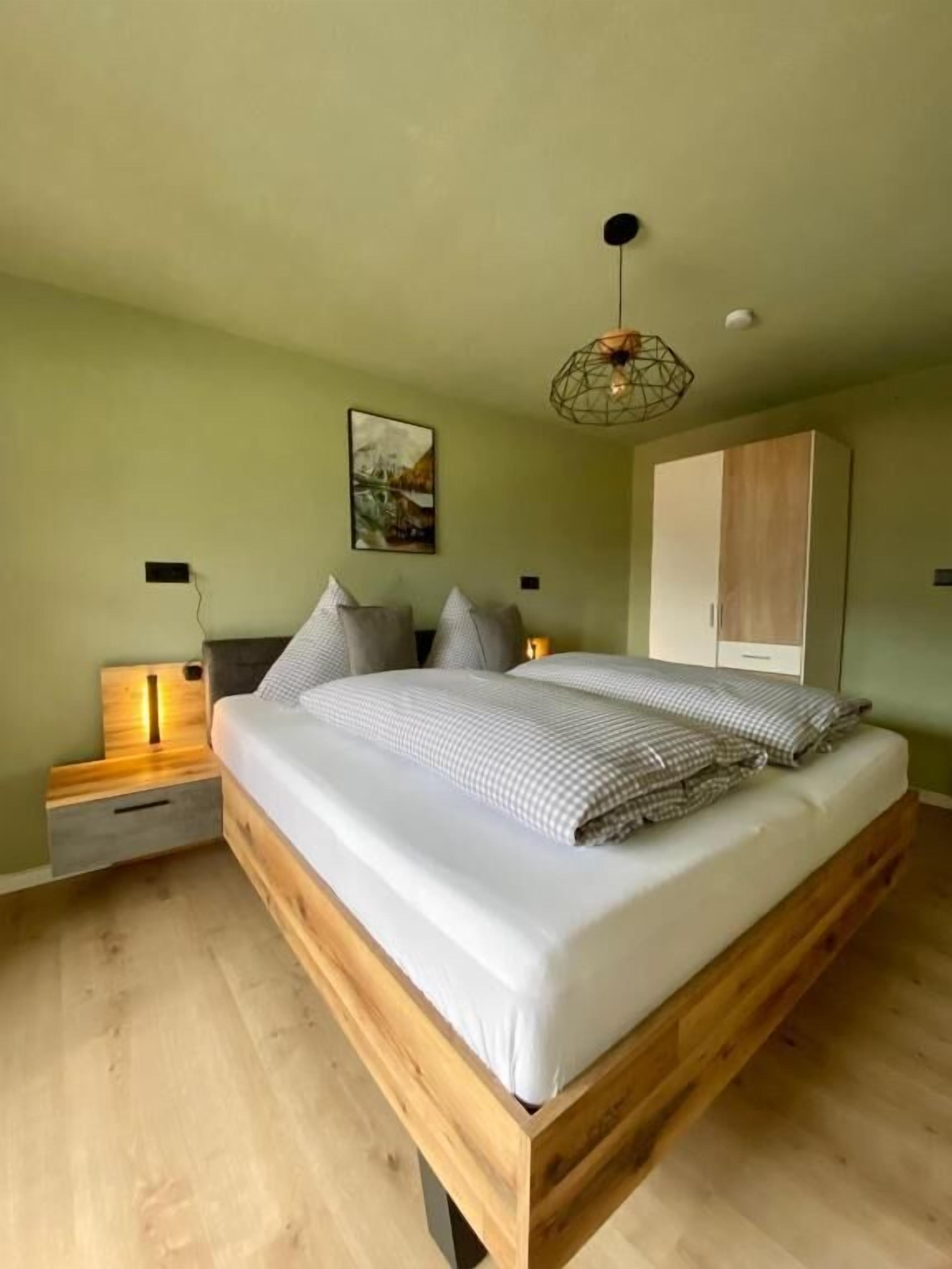 Un dormitorio con una cama de madera, mesitas de noche, un armario y una lámpara colgante.