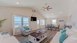 A spacious living area with a view of the ocean, a ceiling fan, and a dining area with chairs and a table. - JL #838 | Deja View | Oceanfront | Ocean Views (Kill Devil Hills)