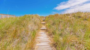 A wooden pathway leading through tall grass towards a building with a wooden fence on the left. - JL #261 | The Beach House | Oceanfront | Ocean Views (South Nags Head)