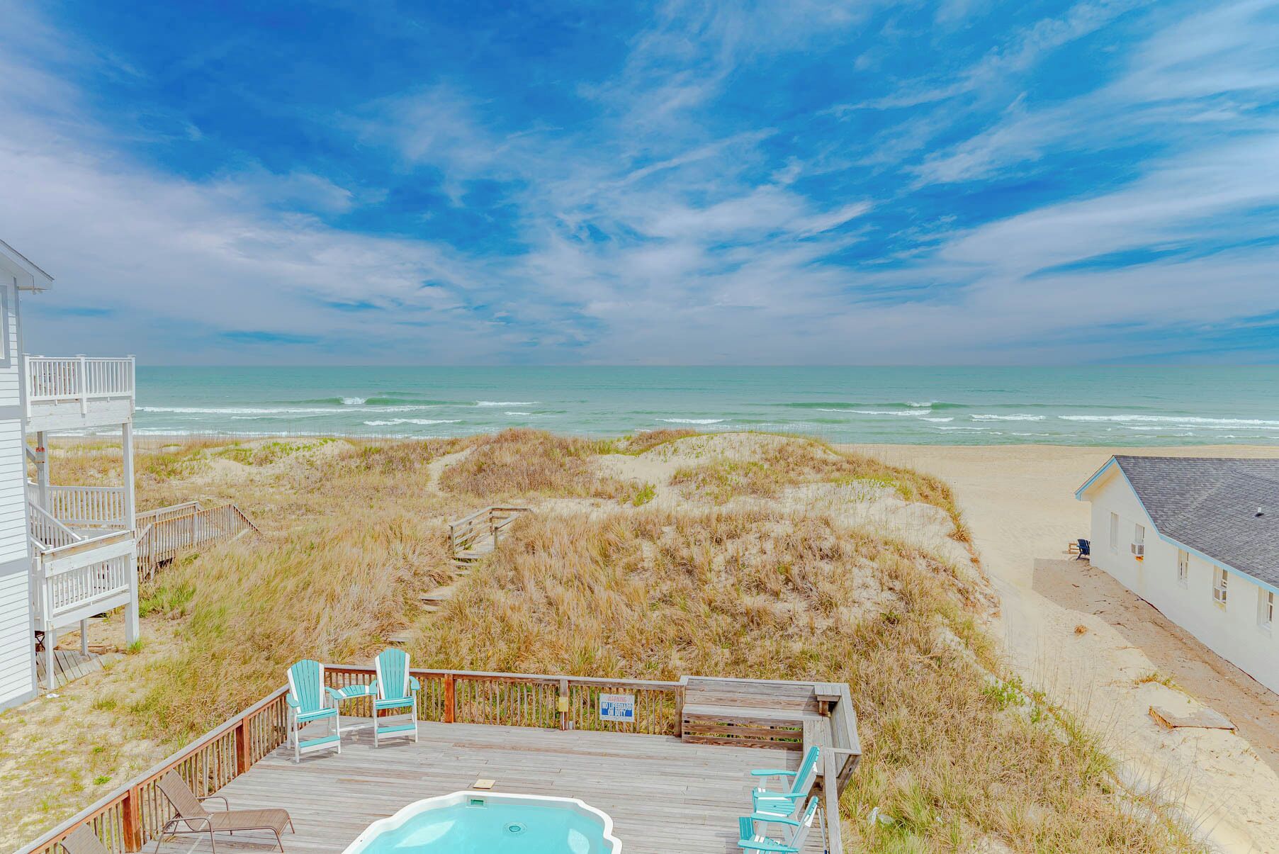 A beach house with a deck, outdoor seating, and a view of the ocean.