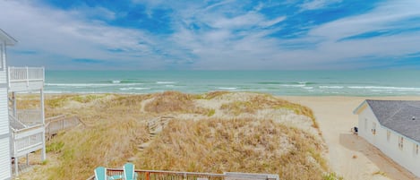 A beach house with a deck, outdoor seating, and a view of the ocean.