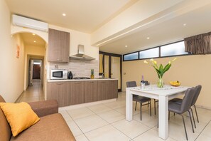 A modern kitchen with a central island, a dining table with chairs, and a living area with a sofa.