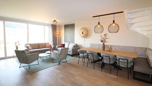 A modern living room with a sofa, chairs, a dining table, and pendant lights. - Luxury Waterfront Villa (Leons)