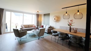 A modern living room with a sofa, chairs, a dining table, and pendant lights. - Luxury Waterfront Villa (Leons)