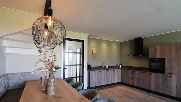 A modern kitchen with wooden cabinets, a built-in oven, and a dining area with a wooden table and chairs. - Luxury Waterfront Villa (Leons)