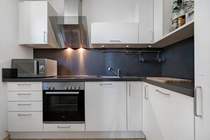 Eine moderne Küche mit weißen Schränken, einem eingebauten Ofen, einer Mikrowelle und einer Spüle aus Edelstahl.