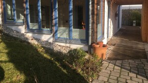 Ein modernes Gebäude mit großen Fenstern, einer Holzterrasse und einem Kiesweg.