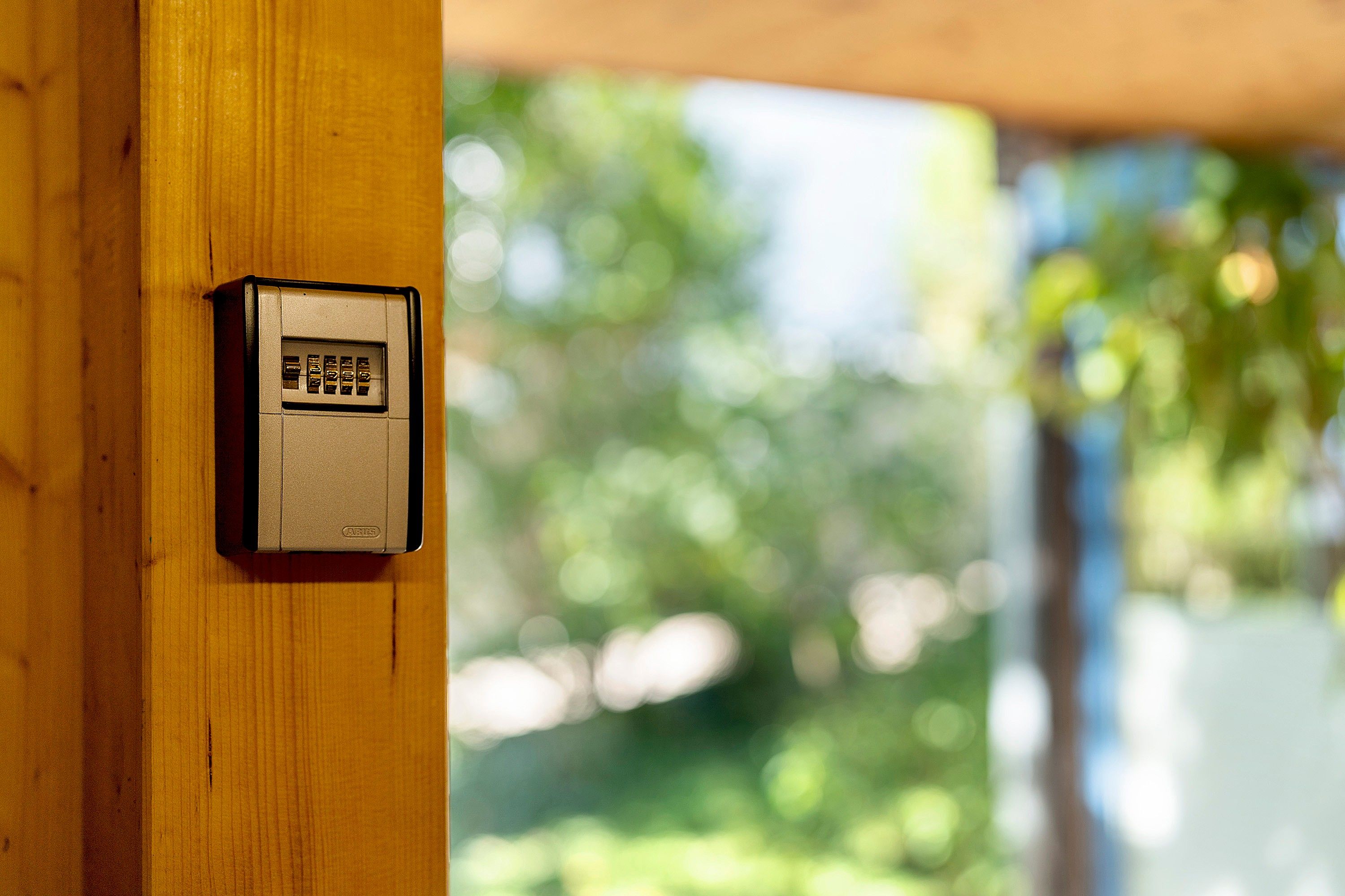 A security keypad mounted on a wooden post, with a blurred green outdoor background.