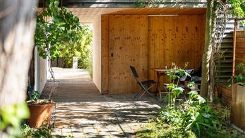 A wooden outdoor seating area with a table and chairs, surrounded by plants and a wooden fence.