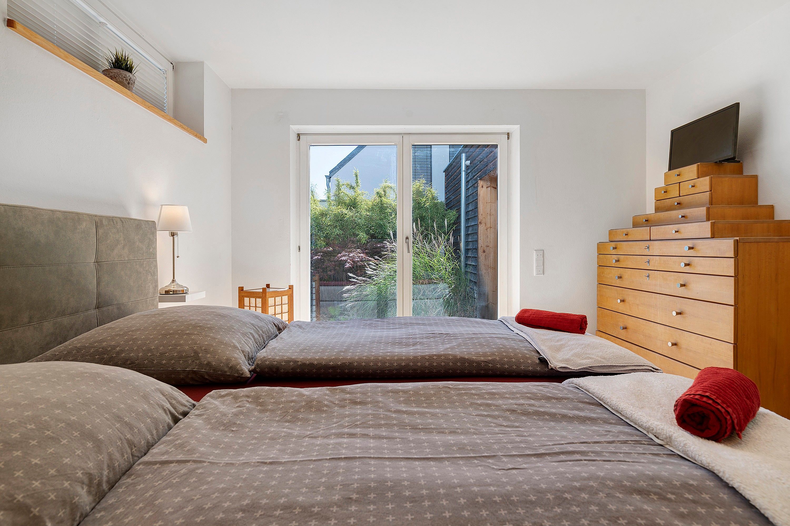 Une chambre à coucher comprenant un lit, une commode en bois, un téléviseur et une fenêtre donnant sur un paysage verdoyant.