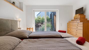 Une chambre à coucher comprenant un lit, une commode en bois, un téléviseur et une fenêtre donnant sur un paysage verdoyant.