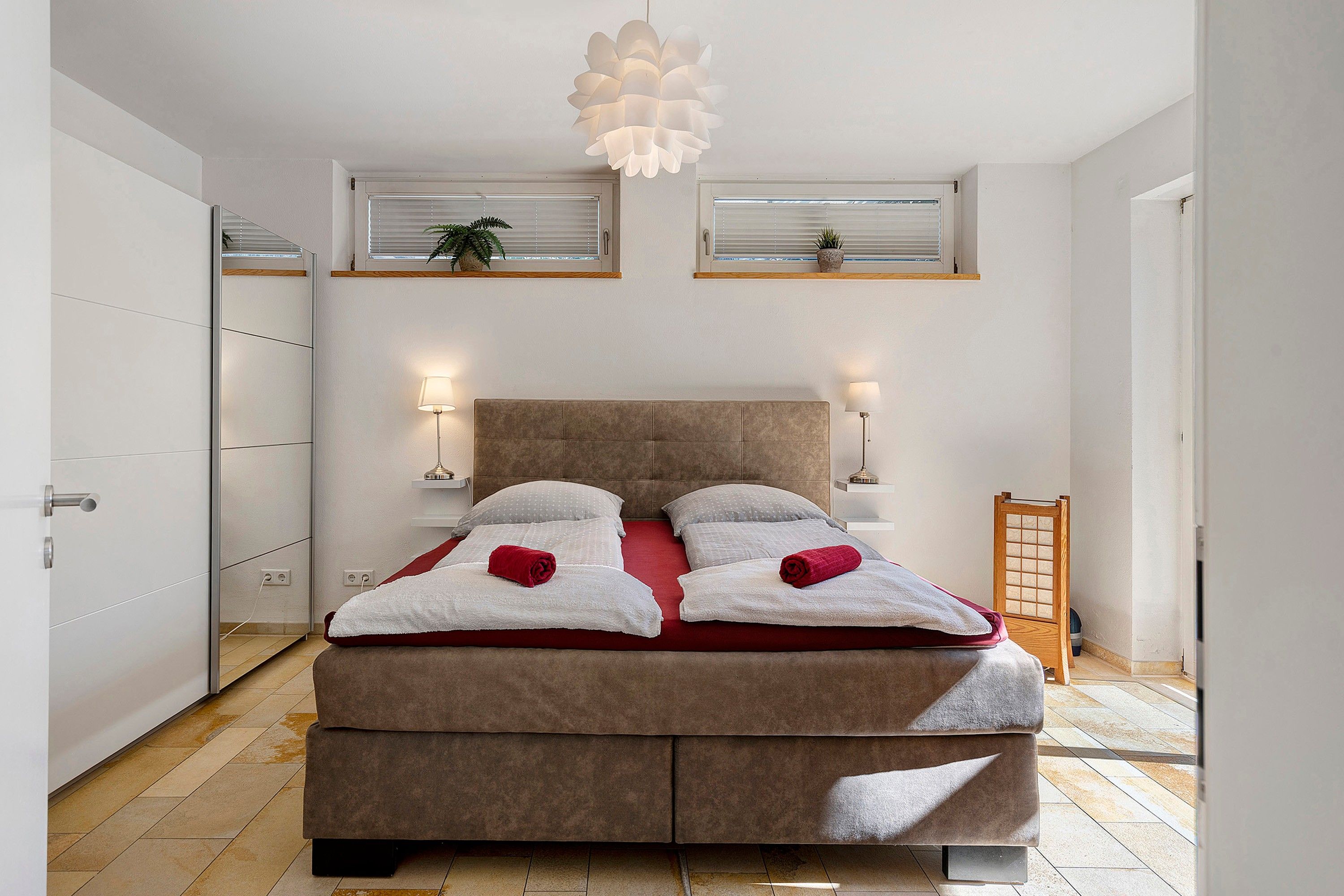 Ein Bett mit Kopfteil, zwei Nachttischlampen und einem Fenster mit Jalousien.