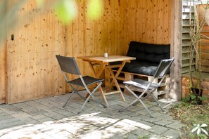 Un espace extérieur aménagé avec des meubles en bois, comprenant une table et deux chaises, un canapé noir et un mur en bois.
