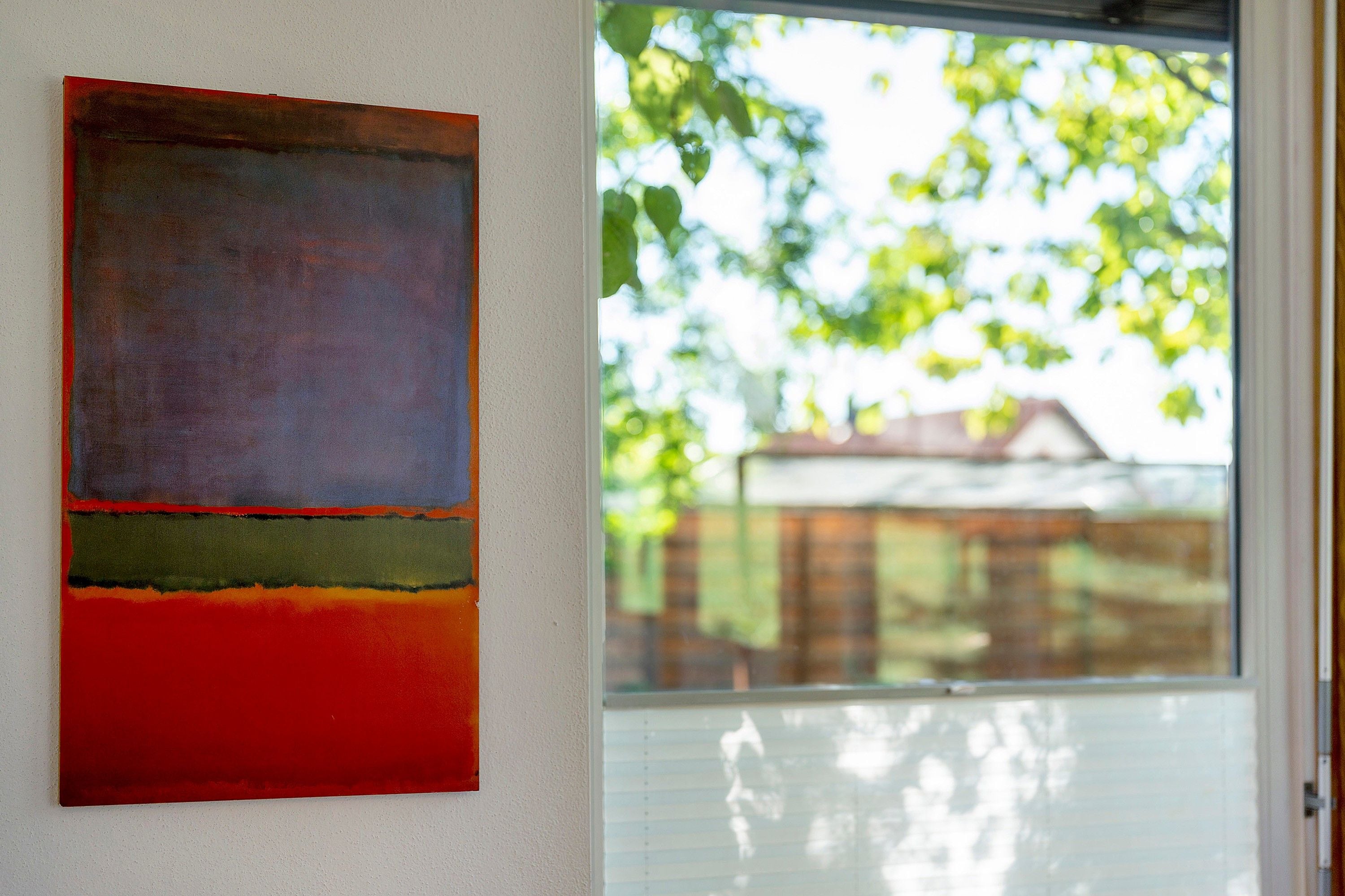 A room with a large abstract painting on the wall and a window with a view of greenery.