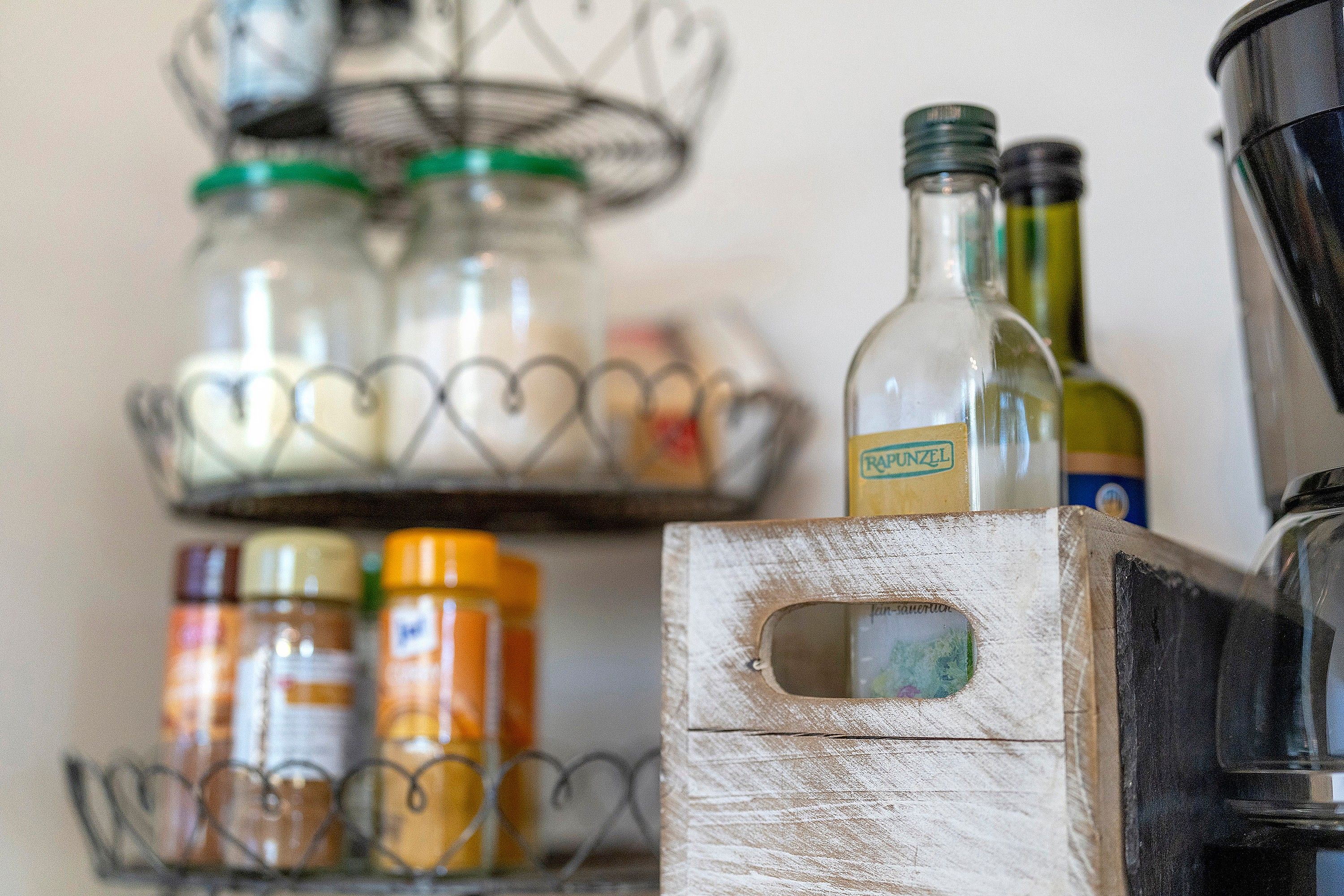A kitchen shelf with jars and bottles, a wooden box, and a metal container.