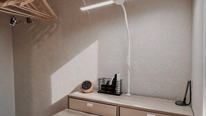 Quarto com escrivaninha, luminária, relógio e um cabideiro.