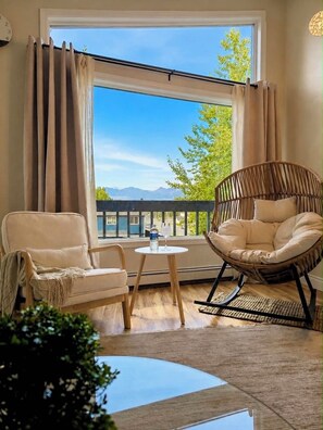 A room with two chairs, a small table, and a view of a balcony and mountains.