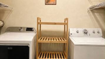 Een wasruimte met twee wasmachines, een houten droogrek en decoratieve muurkunst.