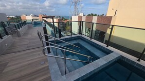 Ein Pool auf dem Dach mit Glasgeländern, einer Holzterrasse und Blick auf die Stadtlandschaft.