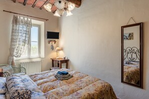 Une chambre à coucher comprenant un lit, une table de chevet avec une lampe, une fenêtre avec des rideaux, une chaise et un miroir fixé au mur.