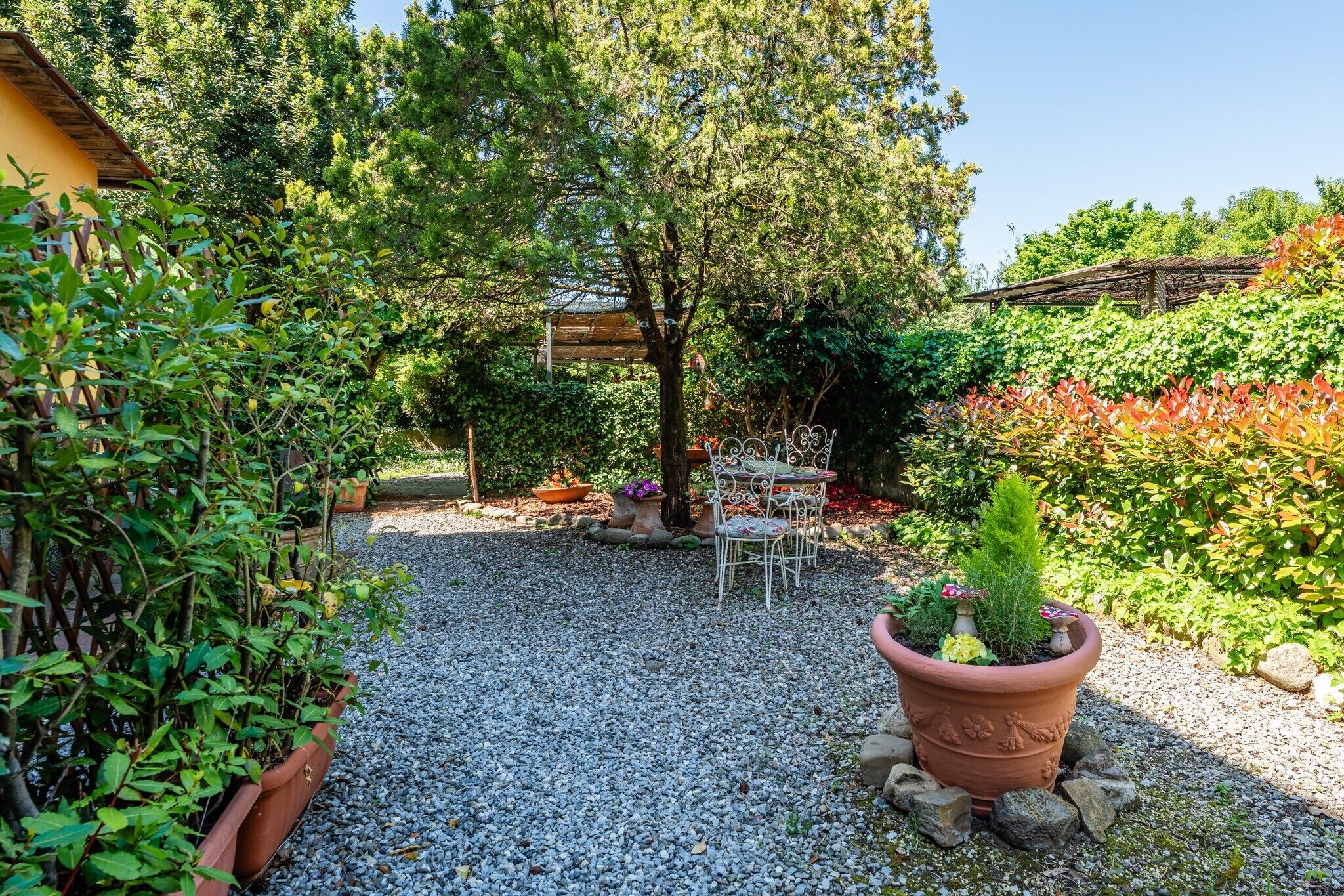 A garden with a gravel path, a wooden pergola, and a seating area with chairs and a table.
