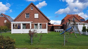 Ein Wohngebiet mit einem Ziegelhaus, einer überdachten Terrasse und einem eingezäunten Garten mit Schaukeln.