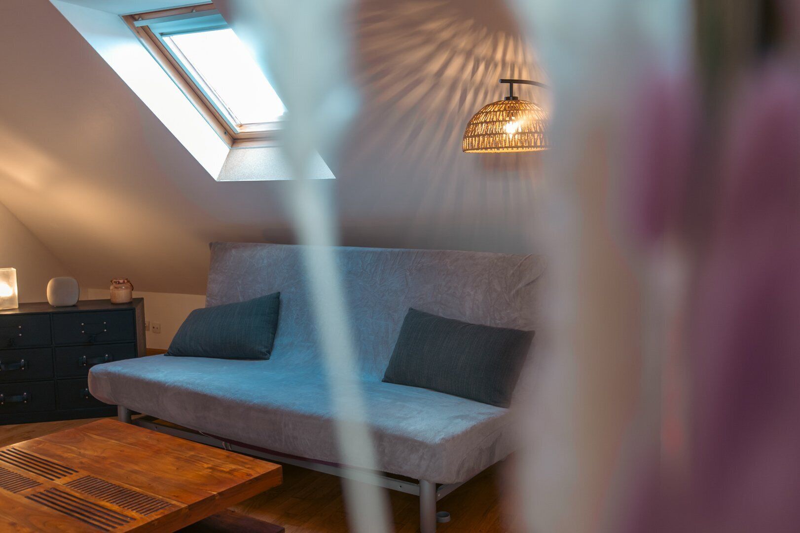 A loft-style bedroom with a skylight, a sofa, a wooden coffee table, and a hanging light fixture.