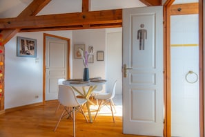 Een eethoek met een ronde tafel, witte stoelen en een vaas met gedroogde bloemen.