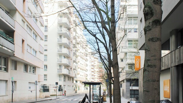 Ein mehrgeschossiges Wohngebäude mit Balkonen, einer Straße davor und einem Baum.