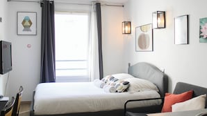 Ein Hotelzimmer mit einem Bett, einem Schreibtisch, einem Sessel, einem Fernseher und Kunstwerken an den Wänden.