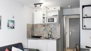 Ein kompakter Wohnraum mit Küchenzeile, Essbereich und einer Couch mit Kissen.