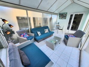 A sunlit patio with a blue sofa, wicker chairs, and a small table. - Jolie Maison De Plage Cyprange Apartment with Private Terrace, Garden, and Wi-Fi (Pirou)