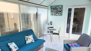 Un espacio de estar con un sofá azul, sillas de mimbre, una mesita y una pared decorada con fotografías.