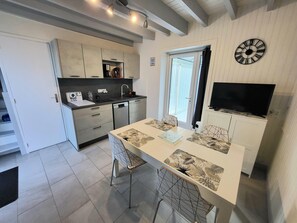 A modern kitchen with a dining area, built-in appliances, and a flat-screen TV. - Jolie Maison De Plage Cyprange Apartment with Private Terrace, Garden, and Wi-Fi (Pirou)