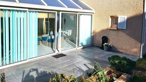 Una casa moderna con un invernadero de vidrio, un patio con mobiliario exterior y un pequeño jardín.