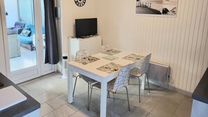 Un comedor con una mesa blanca, sillas, un televisor de pantalla plana sobre un mueble, un reloj y un cuadro en la pared.