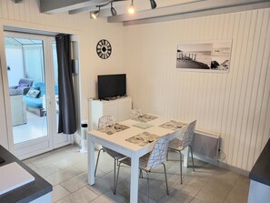 Zona pranzo con tavolo bianco, sedie, televisore a schermo piatto su un mobile, orologio e quadro appeso al muro.