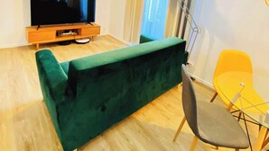 Ett vardagsrum med en grön soffa, en tv, en lampa och en gul stol.