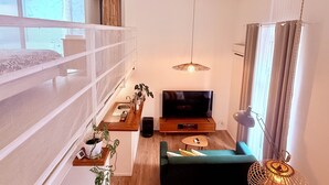 Ett kompakt bostadsutrymme med en våningssäng, en tv, en soffa, ett litet matbord och en hängande lampa.