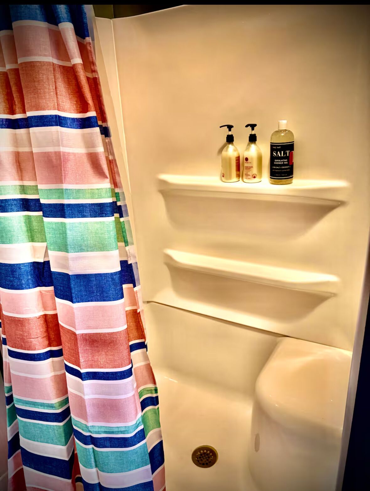 A bathroom with a striped shower curtain, a shelf with two bottles, and a toilet.