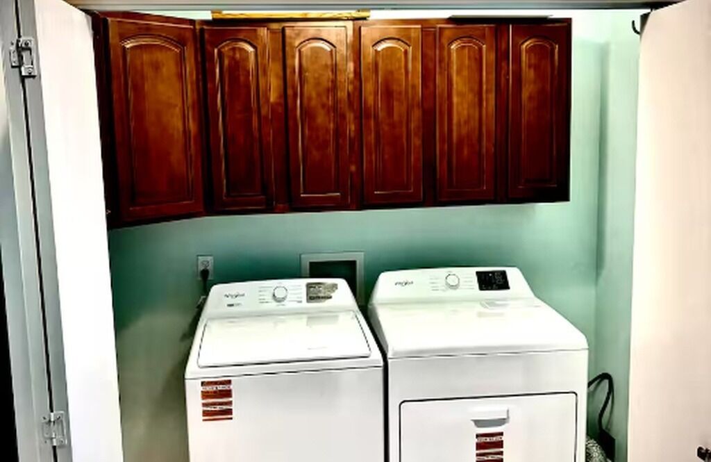 A laundry room with two front-loading washing machines and wooden cabinets above.