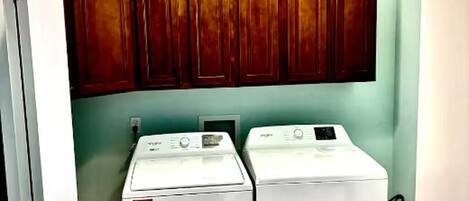 A laundry room with two front-loading washing machines and wooden cabinets above.