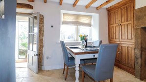 Un comedor con una mesa de madera, sillas, una ventana con cortinas y una pared de piedra.